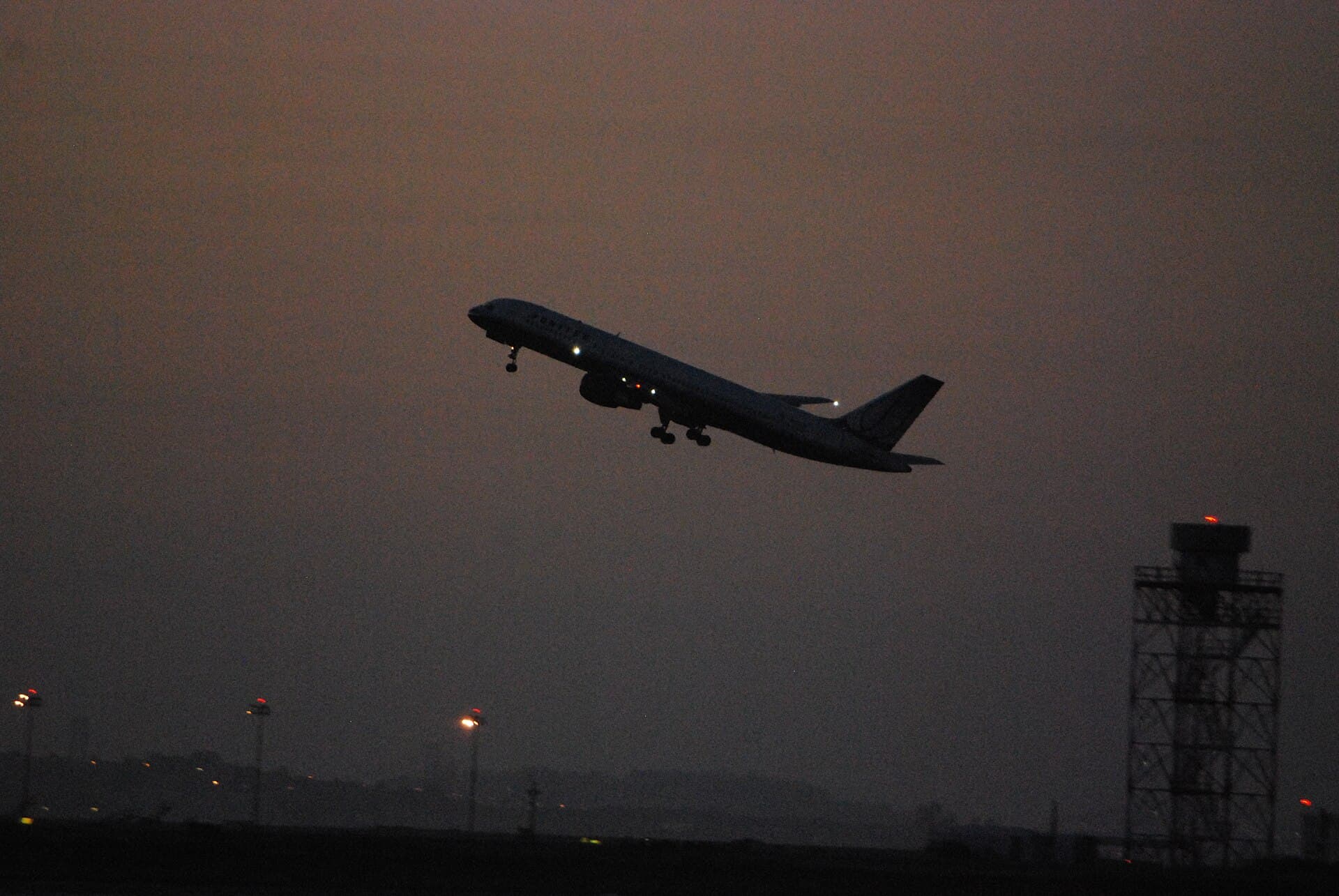 A twin-engine airliner climbing away from the runway in a deep blue dusk sky.