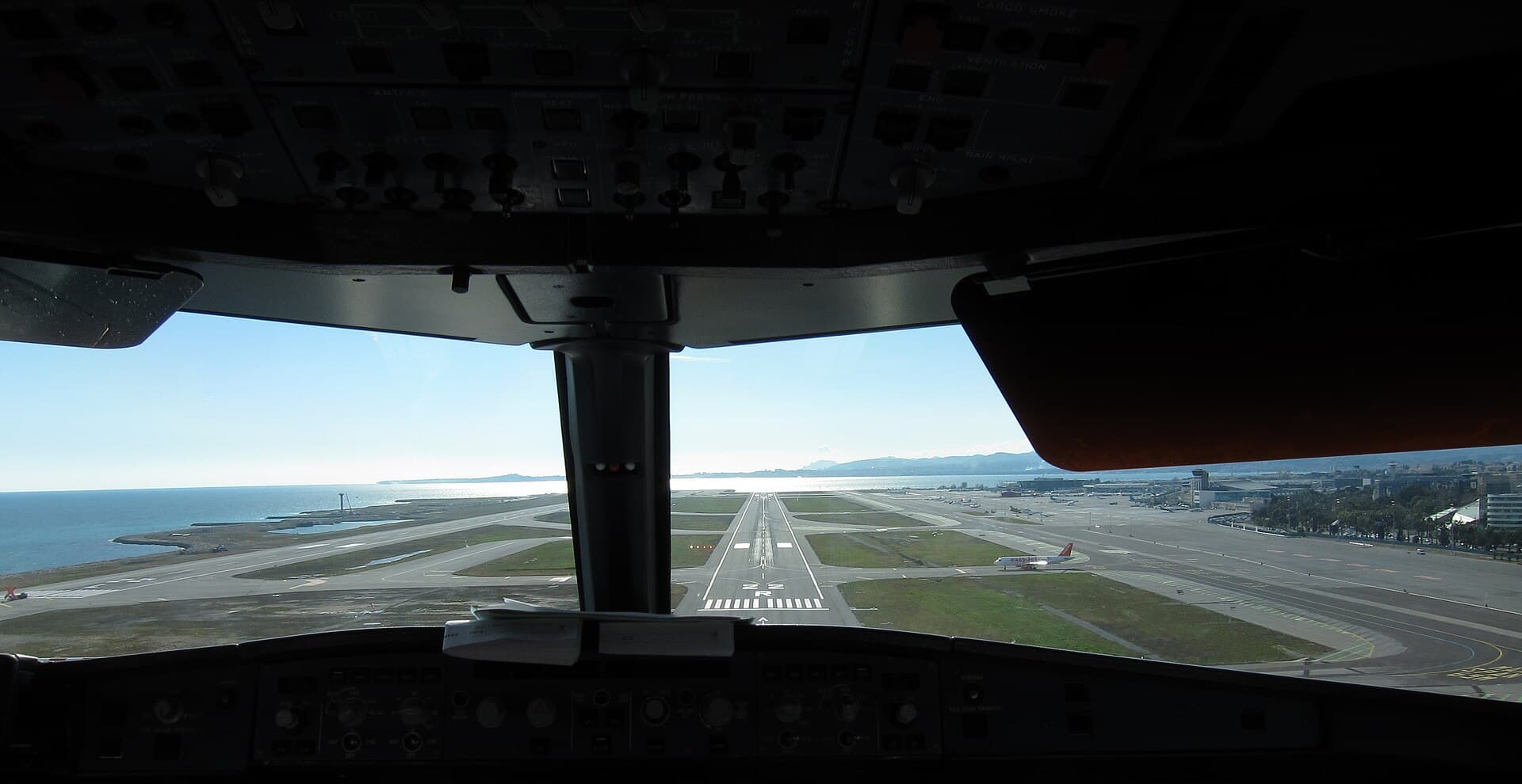 View through a windscreen from the flight deck on short final approach to a runway.